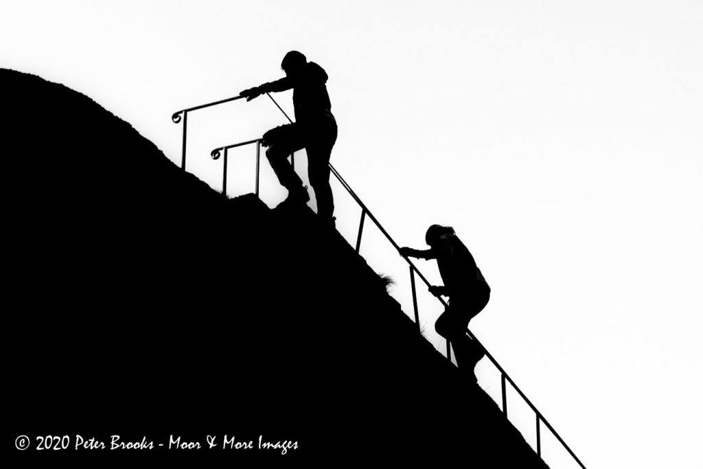 Image of walkers climbing Blackingstone Rock in the style of a linocut.